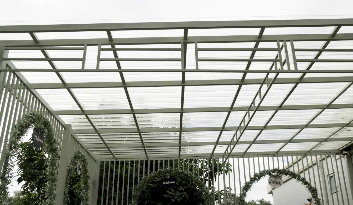 O structură modernă în aer liber, cu un acoperiș geometric transparent și o structură metalică albă. Arcadele circulare acoperite cu frunziș verde creează un decor primitor.